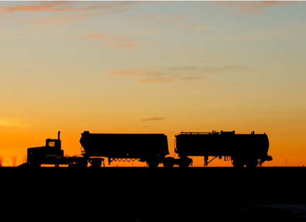Silhouette of a large truck driving on a road at sunrise