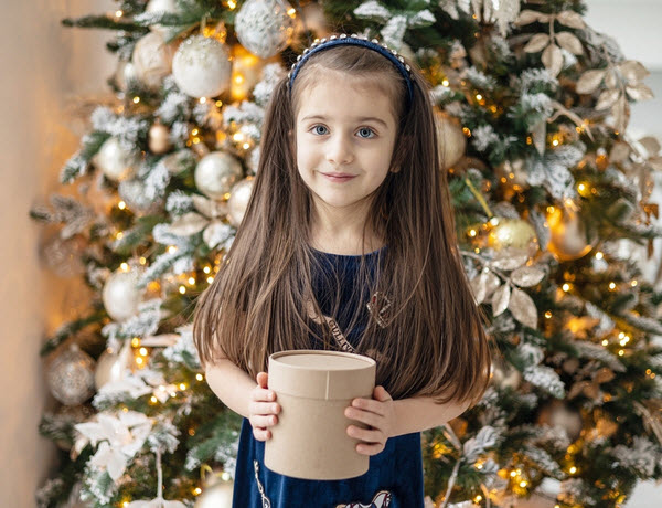 Pretty young lady holding a box of present near the Christmas tree